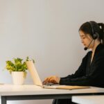 Professional woman engaged in remote work using a laptop with a headset in a modern office.