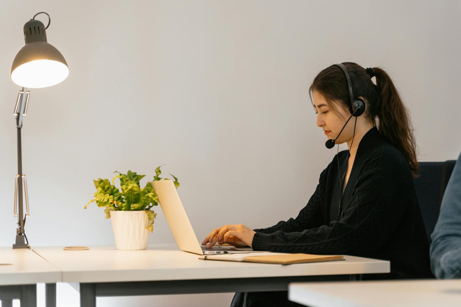 Professional woman engaged in remote work using a laptop with a headset in a modern office.