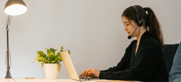 Professional woman engaged in remote work using a laptop with a headset in a modern office.